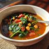 Close-up of a bowl of Vegan Chickpea & Spinach Soup with chickpeas, spinach, and tomatoes.