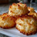 A close-up of golden-brown whipped shortbread cookies stacked on a white plate, showcasing their textured surface.