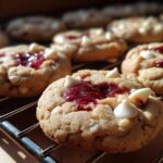 Close-up of freshly baked White Chocolate Raspberry Thumbprint Cookies on a cooling rack, with raspberry jam filling.