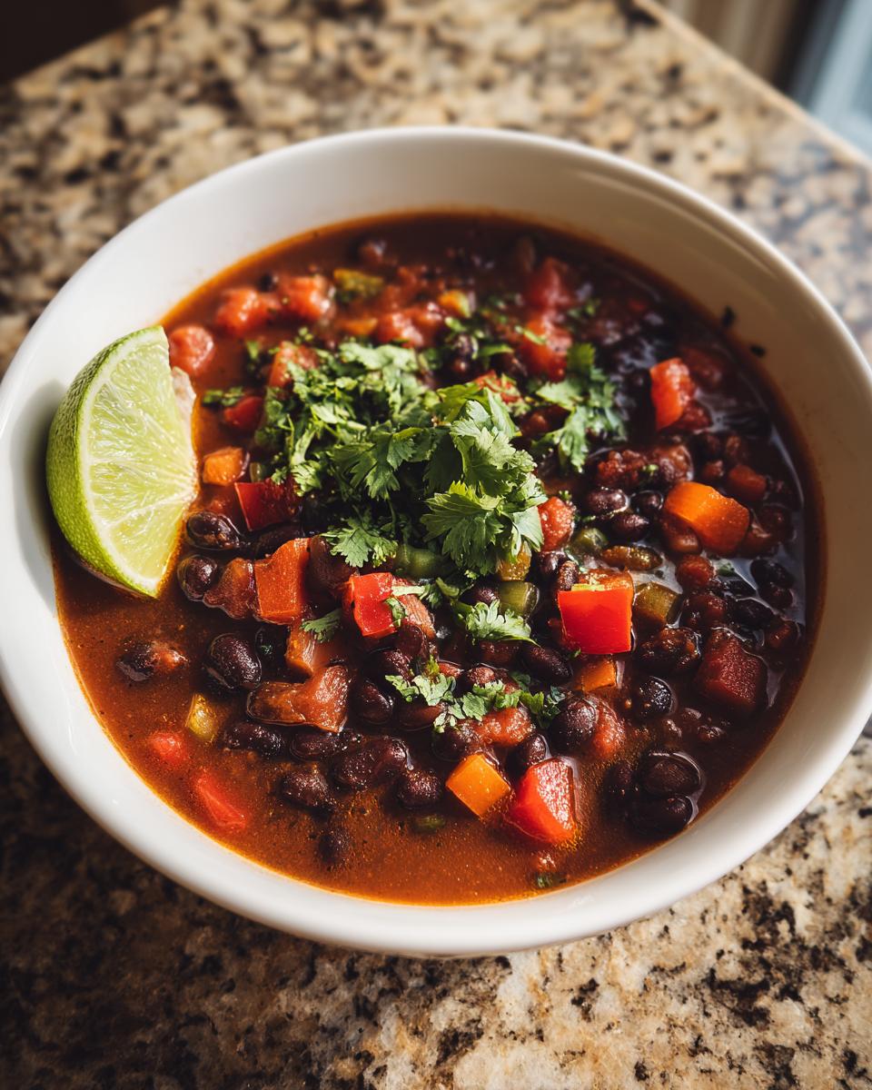 Close-up of a bowl of zesty black bean soup, garnished with cilantro and a lime wedge.