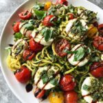 A colorful plate of Zucchini Noodle Pesto Caprese with tomatoes, mozzarella, and pesto.