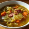Close-up of a bowl of Cabbage and Kielbasa Soup, with visible cabbage, carrots, and sausage.