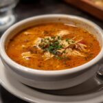 Close-up of a bowl of Carrabba's Copycat Chicken Soup, garnished with fresh herbs.