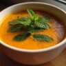 Close-up of a bowl of Carrot Ginger Mint Soup garnished with fresh mint leaves.
