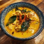 Close-up of a bowl of Easy Thai Chicken Curry Soup with chicken, herbs, and chili.