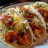 Close-up of three delicious spicy shrimp tacos, ready to eat. One bite and you'll understand the hype!