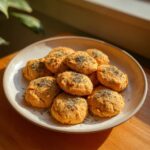 A plate of homemade catnip-infused cat treats, sprinkled with herbs, on a wooden surface.