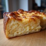 Close-up of a slice of Foolproof Cheese Soufflé, golden brown and fluffy on a wooden board.
