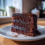 A slice of decadent double chocolate cake with rich chocolate frosting on a white plate.
