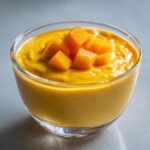 Close-up of a glass of Delicious Mango Pudding topped with fresh mango chunks.