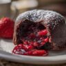 Close-up of a Strawberry Chocolate Lava Dome with oozing strawberry filling, dusted with powdered sugar.