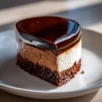 A slice of Triple Chocolate Mousse Cake with a silky mirror glaze on a white plate.