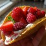 Close-up of a Berrylicious Cheesecake Taco filled with cream and topped with fresh berries.