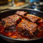 Close-up of braised short ribs with red wine simmering in a pan, showcasing the tender meat.