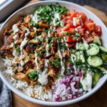A colorful Chicken Shawarma Bowl with rice, chicken, tomatoes, cucumbers, and a creamy sauce.