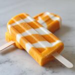 Two delicious Coconut Mango Popsicles with a checkered pattern, resting on a marble surface.