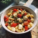 A bowl of Creamy Caprese Pasta Salad with tomatoes, mozzarella, and herbs.