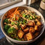 Close-up of a Crispy Tofu Buddha Bowl with tofu, quinoa, broccoli, carrots, and sauce.