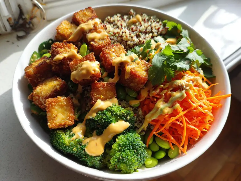 A colorful Crispy Tofu Buddha Bowl with tofu, quinoa, broccoli, carrots, and a creamy sauce.
