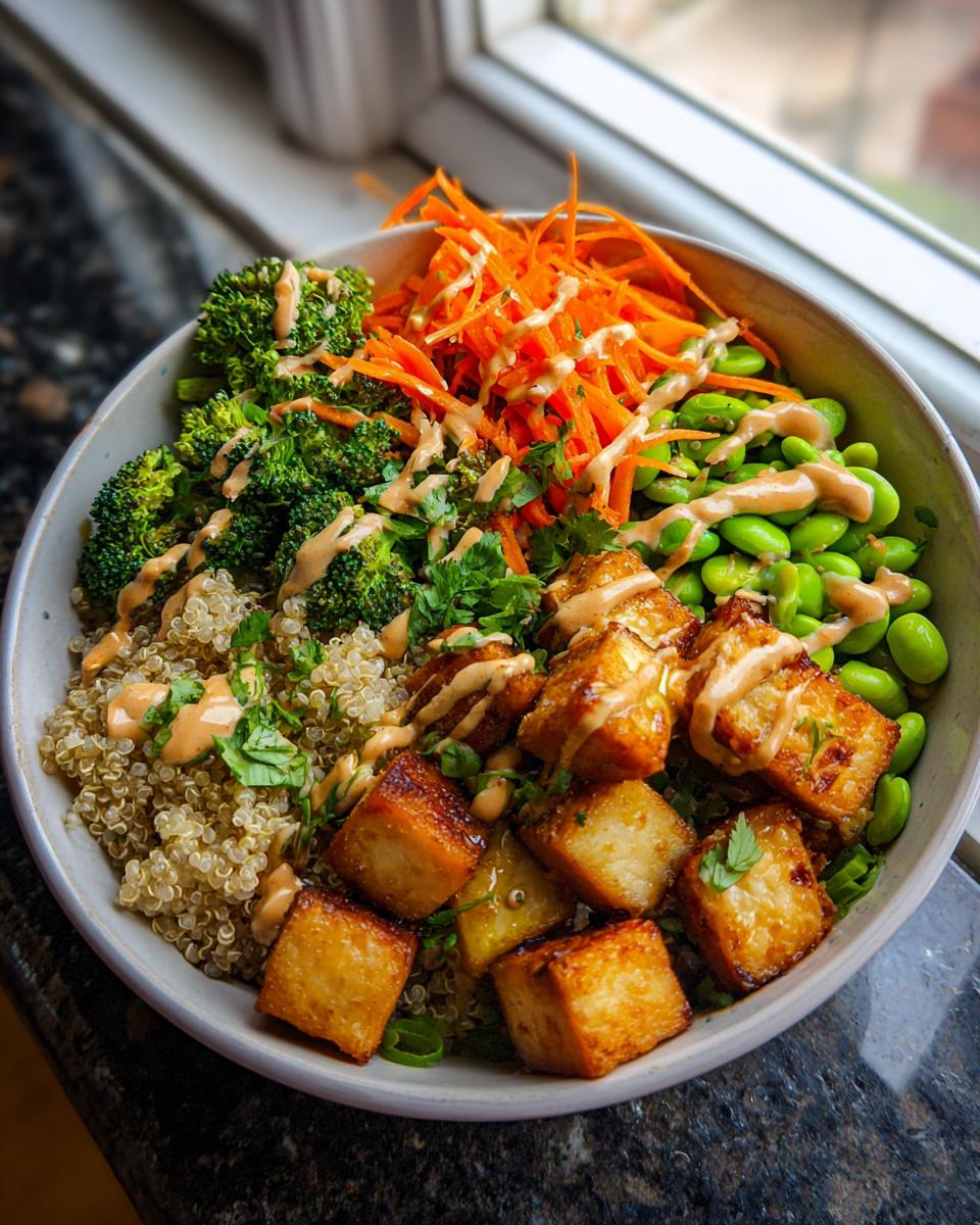 A vibrant Crispy Tofu Buddha Bowl with quinoa, broccoli, carrots, edamame, and a creamy sauce.