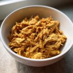 Close-up of shredded Crockpot Chicken Recipes Healthy in a white bowl, ready to eat.