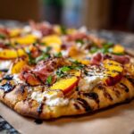 Close-up of a delicious Grilled Peach & Prosciutto Pizza with peaches, prosciutto, and basil.