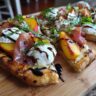Close-up of a Grilled Peach & Prosciutto Pizza with fresh basil and balsamic glaze.