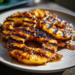 Close-up of grilled pineapple rings on a plate, drizzled with cinnamon butter.