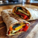 Close-up of a Grilled Veggie & Hummus Wrap cut in half, showing grilled vegetables.