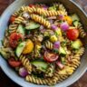 Overhead shot of a vibrant pasta salad with tomatoes, cucumber, red onion, and herbs. This is a healthy pasta salad recipe.