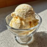 Scoops of creamy Honey Lavender Ice Cream in a glass dessert bowl, lit by sunlight.
