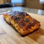 Close-up of a perfectly cooked Honey Mustard Glazed Salmon fillet on a wooden cutting board.