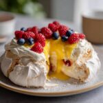 Close-up of a Lemon Curd Pavlova dessert topped with fresh berries and whipped cream.