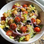 Close-up of a delicious Olive Garden Salad with tomatoes, olives, red onion, and croutons.