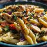 Close-up of a bowl of pasta salad and chicken with vegetables and herbs.