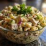 Close-up of a pasta salad and chicken in a glass bowl, with pasta, chicken, red onion, and parsley.