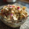 Close-up of a bowl of pasta salad and chicken with red onion and herbs. The pasta salad and chicken is creamy.