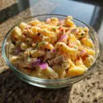 Close-up of a bowl filled with pasta salad and chicken, with red onion and spices.