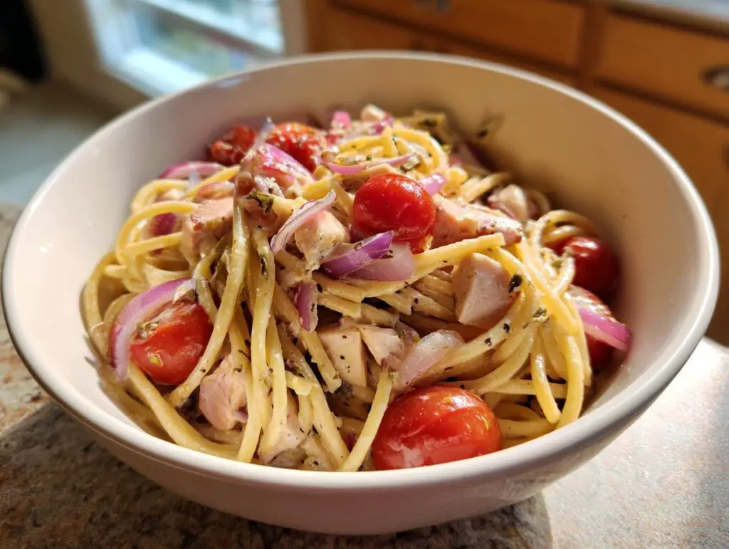 Close-up of a bowl of pasta salad and chicken with tomatoes and red onion.