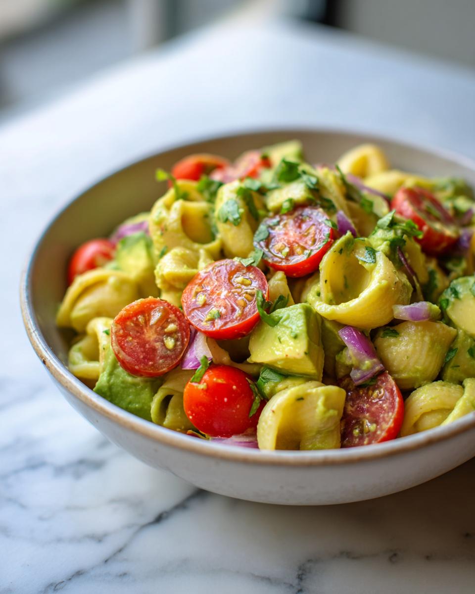 Close-up of pasta salad avocado in a bowl with tomatoes and red onion.