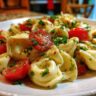 Close-up of pasta salad using cheese tortellini with tomatoes and herbs on a white plate.