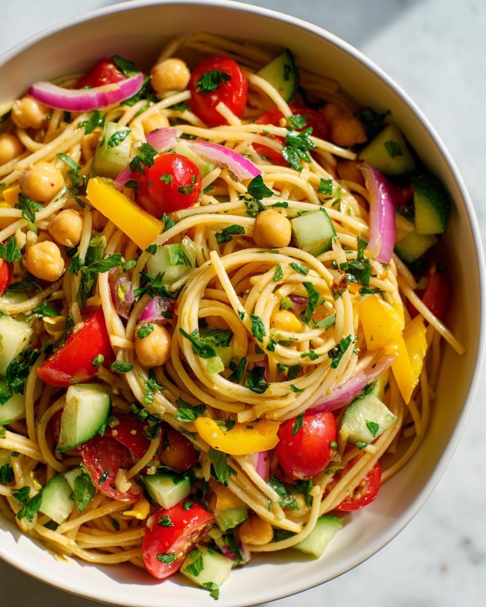 Amazing pasta salad chickpeas in 25 minutes 8 Overhead shot of a delicious pasta salad chickpeas in a white bowl, with fresh vegetables and herbs.