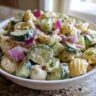 Close-up of a bowl of pasta salad cucumber, with pasta, cucumber, red onion, and dill.