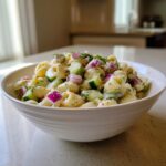 Pasta salad cucumber in a white bowl, with pasta, cucumber, red onion, and dill.