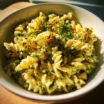 Close-up of pasta salad dill pickle in a white bowl, garnished with fresh dill.