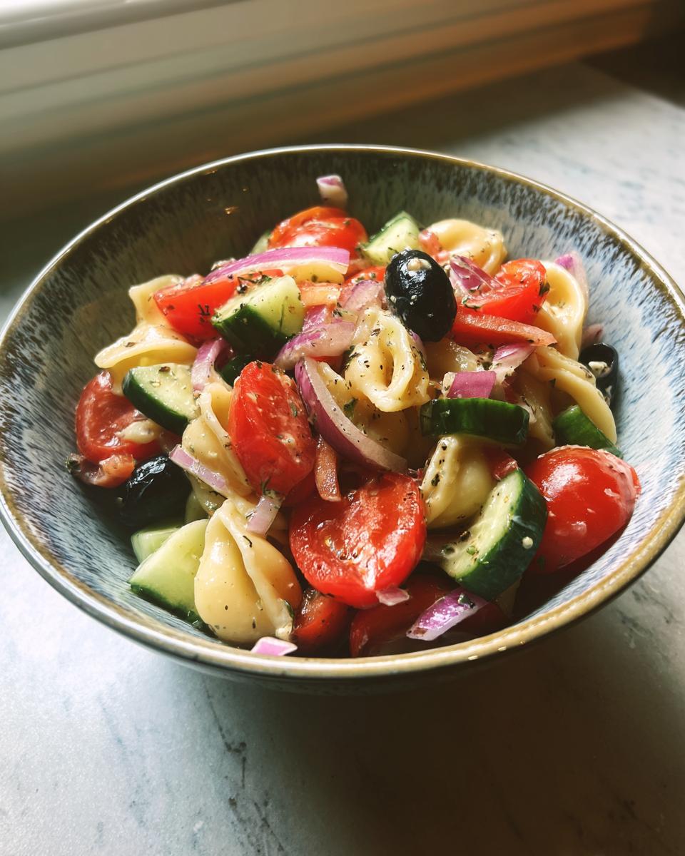 Close-up of a bowl of pasta salad easy simple with tomatoes, cucumbers, olives, and red onion.