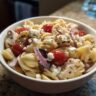 A bowl of delicious pasta salad high protein with chicken, tomatoes, feta, and red onion.