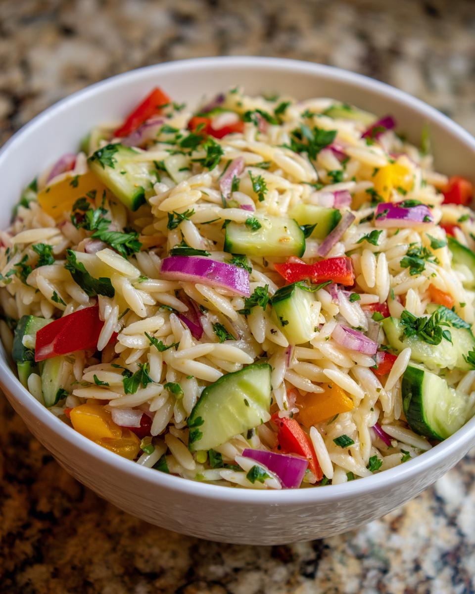 Amazing pasta salad orzo: 30-min delight 9 Close-up of a vibrant pasta salad orzo with cucumbers, peppers, and red onion in a white bowl.