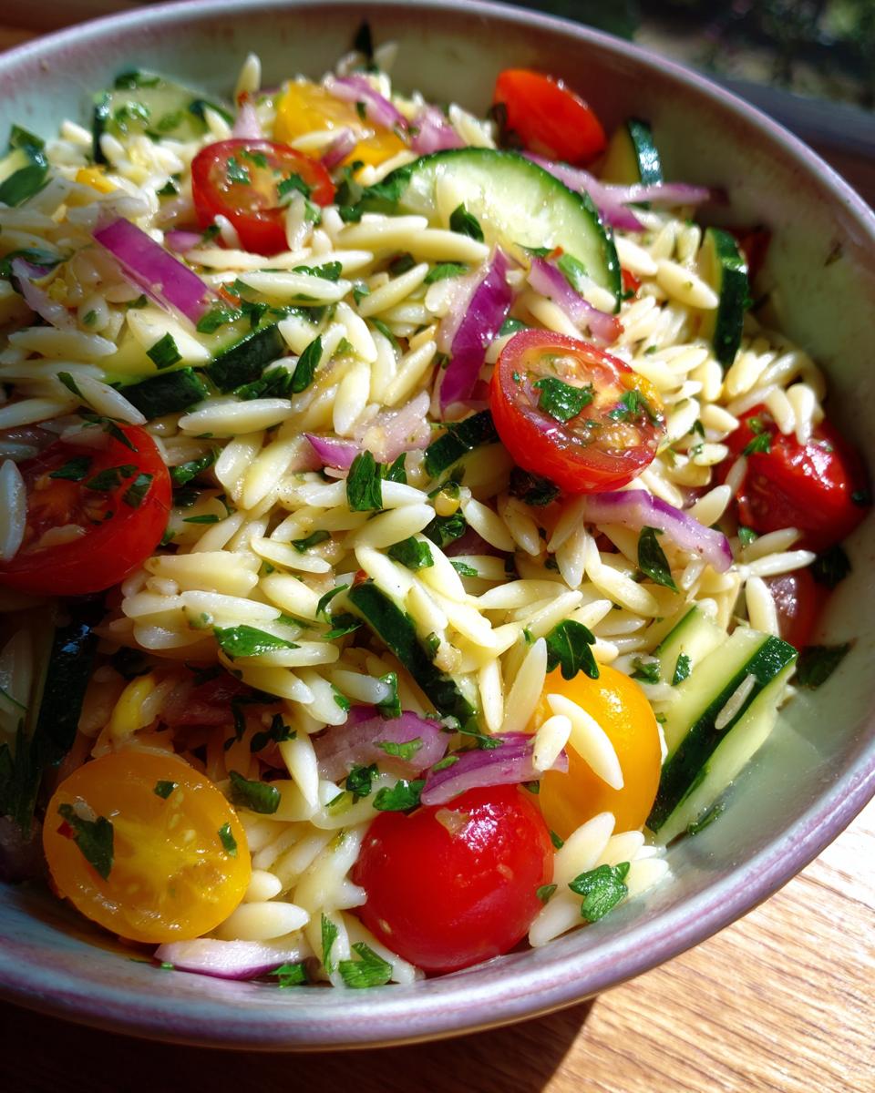 Amazing pasta salad orzo: 25 min summer favorite 8 Close-up of pasta salad orzo with cherry tomatoes, cucumbers, red onion, and herbs.