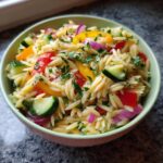 Amazing pasta salad orzo: 30-min delight 11 Close-up of a bowl of pasta salad orzo with cucumbers, bell peppers, red onion, and herbs.